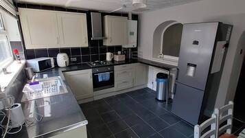 A modern kitchen with white cabinets, a stainless steel countertop, a built-in oven, a microwave, a coffee maker, and a refrigerator.