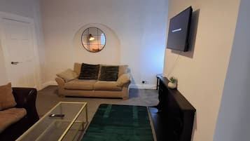 Uma sala de estar com sofá, mesa de centro, televisão e um espelho decorativo.