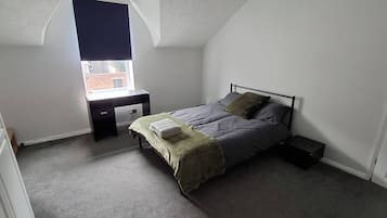 A bedroom with a bed, a desk, and a window.
