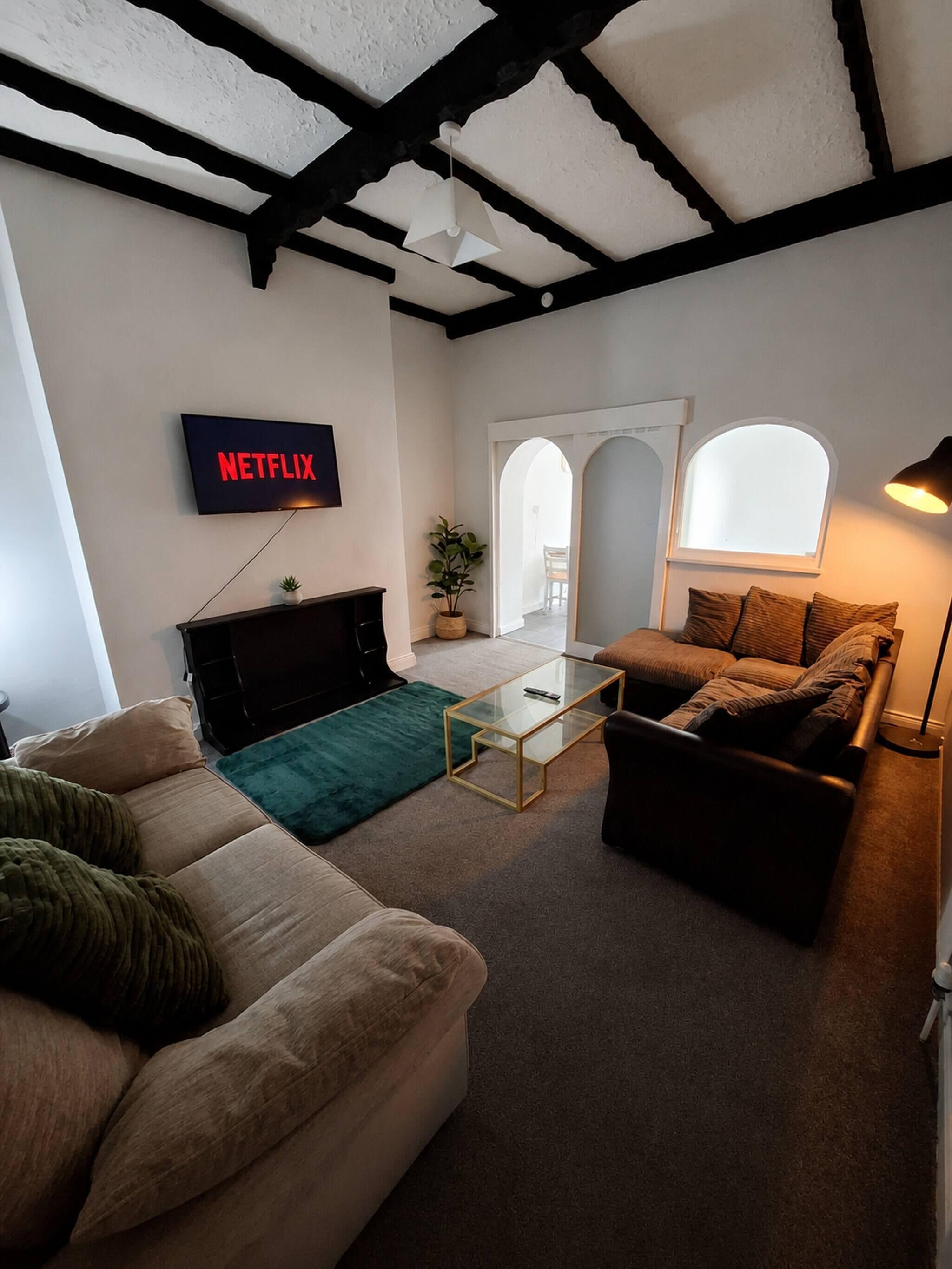 Una sala de estar con una televisión mostrando 'NETFLIX', un sofá, una mesa de centro y una lámpara.