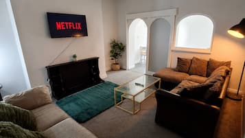 Una sala de estar con una televisión mostrando 'NETFLIX', un sofá, una mesa de centro y una lámpara.