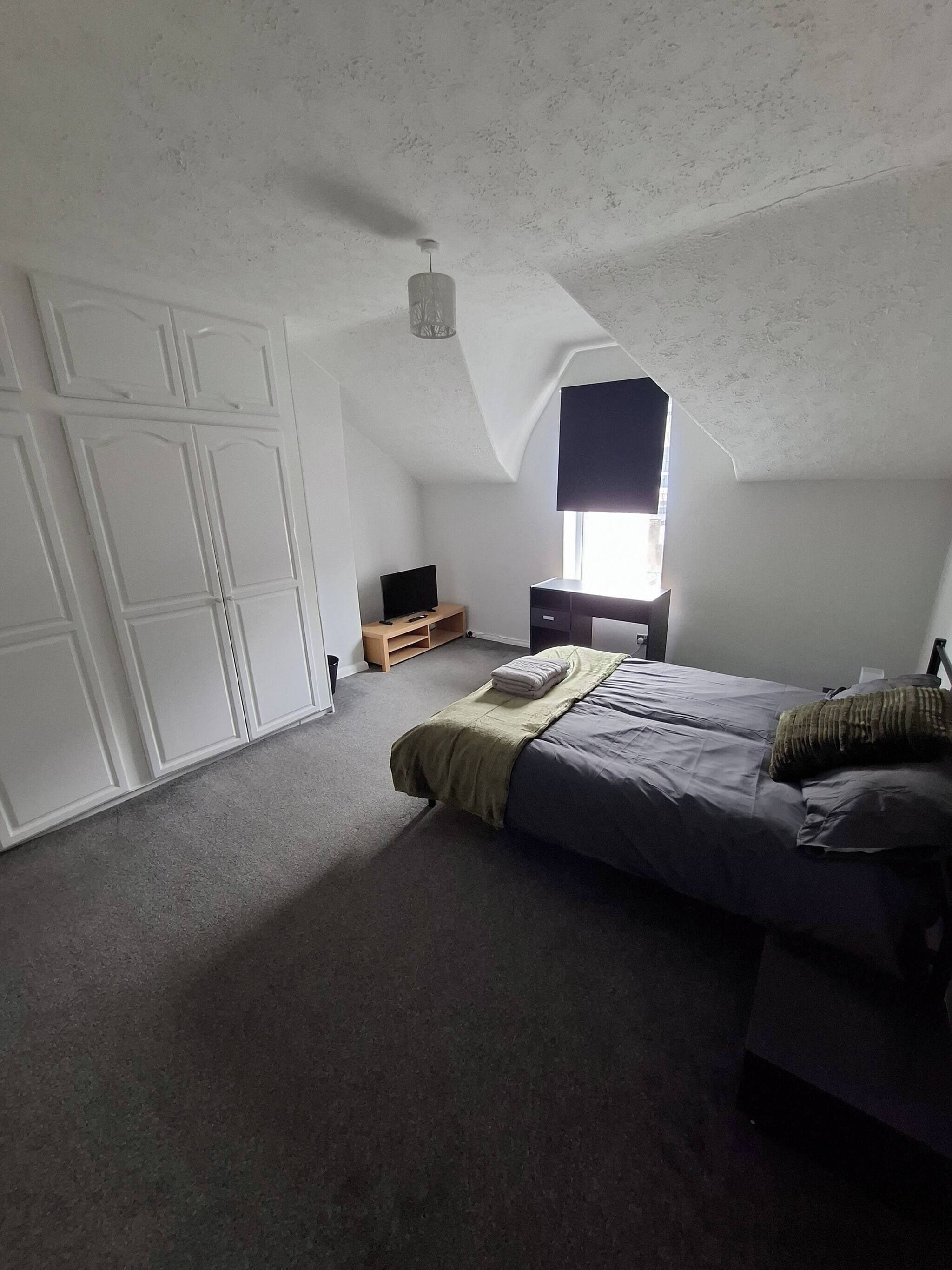 Quarto com cama, televisão, guarda-roupa e janela.