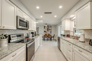 A modern kitchen with white cabinetry, a stainless steel range, and a dining area with a table and chairs. - Villa Laetitia-on water, pool, boat dock (Cape Coral)