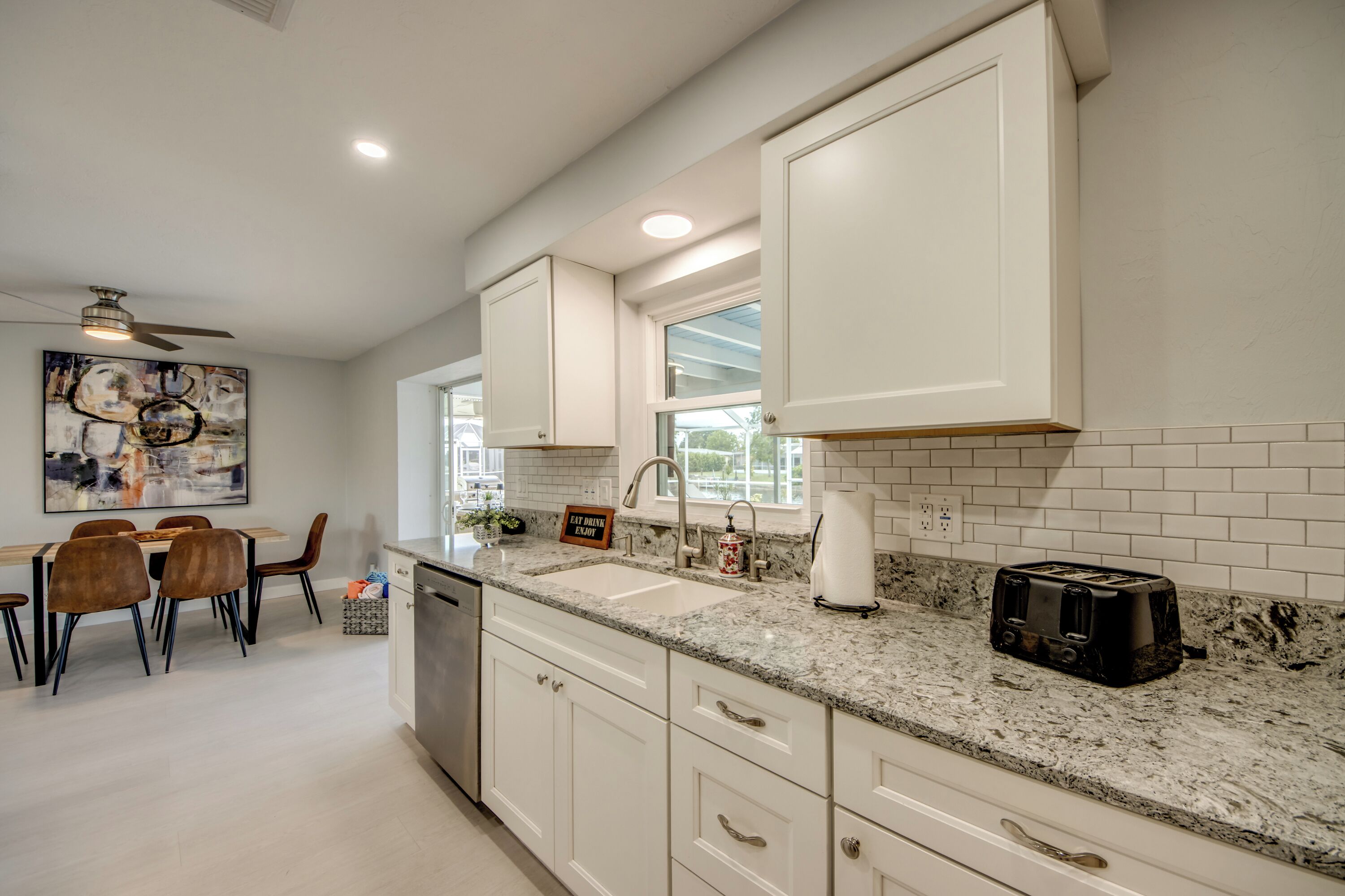 A modern kitchen with white cabinetry, a granite countertop, and a dining area with a table and chairs.