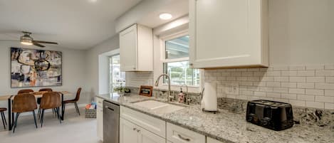 A modern kitchen with white cabinetry, a granite countertop, and a dining area with a table and chairs.