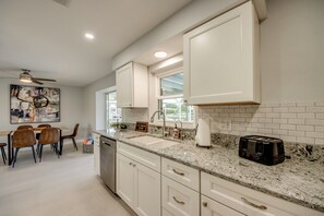 Une cuisine moderne avec des meubles blancs, un plan de travail en granit et un coin repas comprenant une table et des chaises.