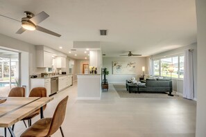 A modern kitchen with white cabinets, a dining area with a wooden table and chairs, and a living room with a grey sofa and a painting on the wall. - Villa Laetitia-on water, pool, boat dock (Cape Coral)