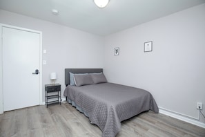 Um quarto com uma cama, mesa de cabeceira, abajur e porta.