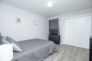 A bedroom with a bed, a dresser, a television, and a door. - Stylish 2Bed 2 Bath, Laundry, Gated Backyard, Smart Lock, Unit 2 (East Orange)