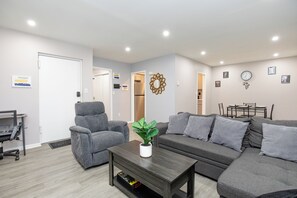 A modern living room with a grey sofa, armchairs, a coffee table with a plant, and a dining area with a table and chairs. - Stylish 2Bed 2 Bath, Laundry, Gated Backyard, Smart Lock, Unit 2 (East Orange)