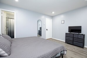 A bedroom with a bed, a dresser, a TV, and a door. - Stylish 2Bed 2 Bath, Laundry, Gated Backyard, Smart Lock, Unit 2 (East Orange)