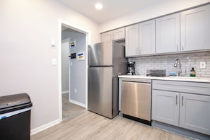 Cozinha moderna com eletrodomésticos de aço inoxidável, armários cinza e painel de azulejos.