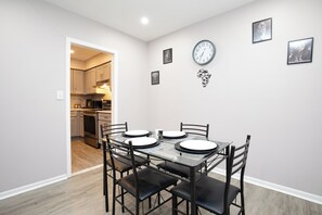 A dining area with a table set for four, a clock on the wall, and framed pictures. - Stylish 2Bed 2 Bath, Laundry, Gated Backyard, Smart Lock, Unit 2 (East Orange)