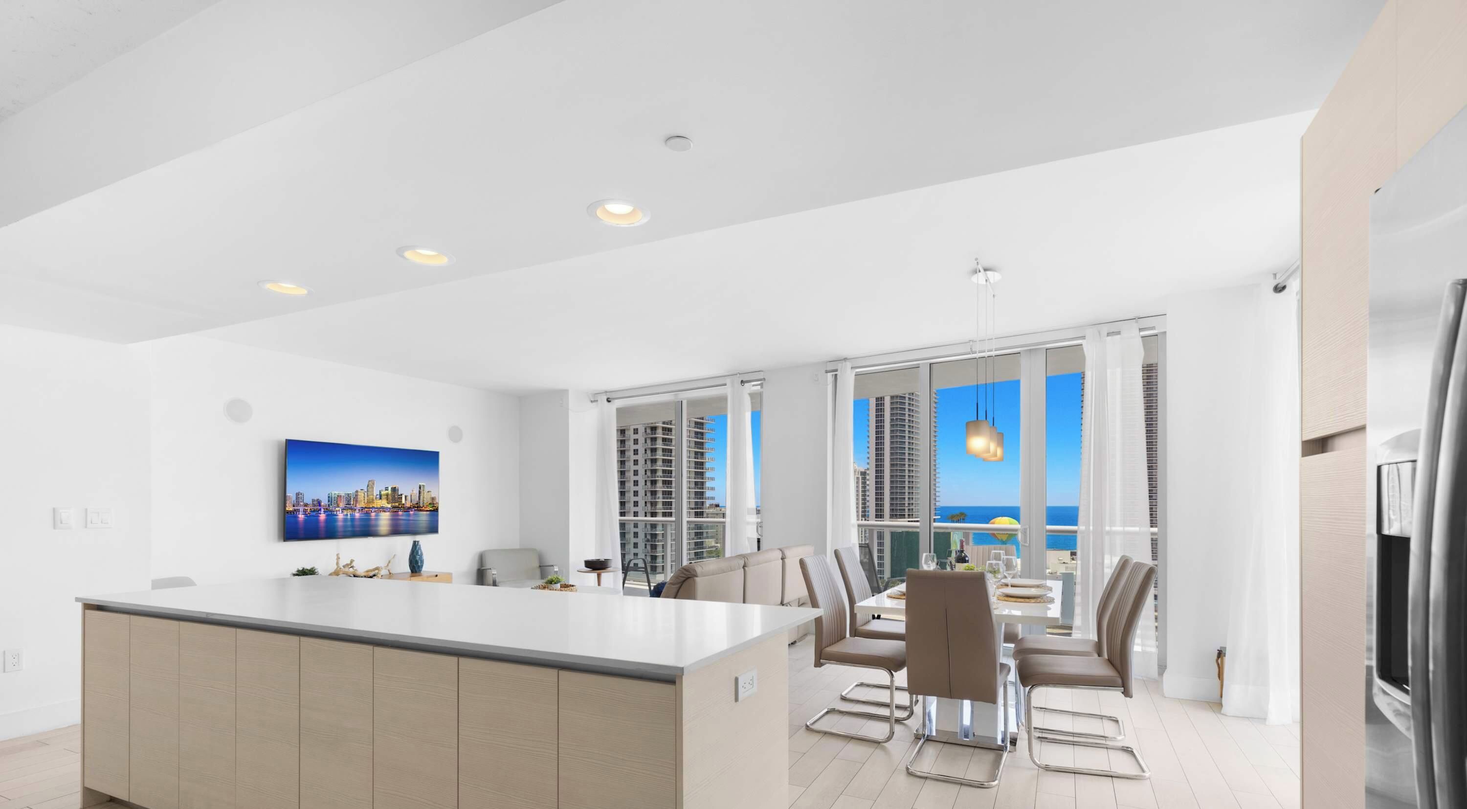 Een moderne keuken met een centraal eiland, een eetgedeelte met stoelen en grote ramen met uitzicht op de stadshemel.