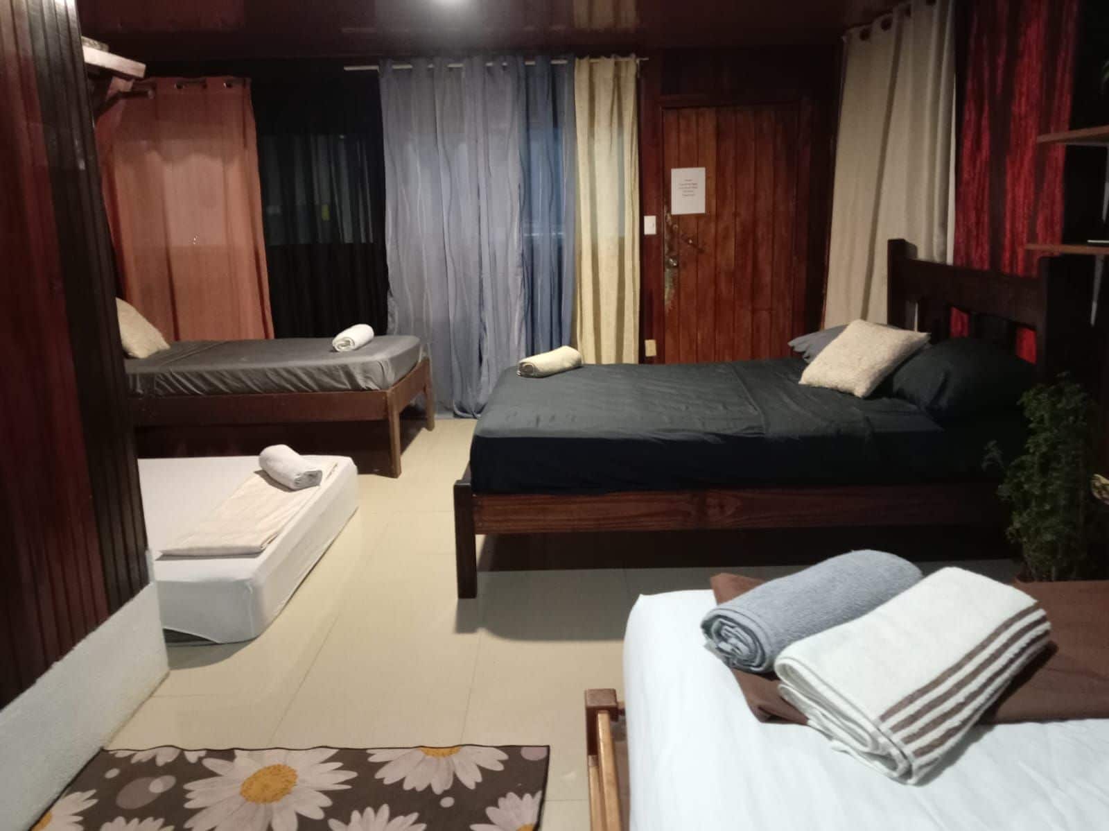 A room with two beds, a wooden headboard, a small table, and a curtain.