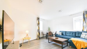 A modern living room with a sofa, coffee table, and a dining area with chairs and a table. - Evasion Mulhousienne - 2-bedroom apartment with AC, Wi-Fi, and free parking (Mulhouse)