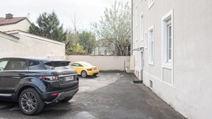 A parking area with two cars, a black SUV and a yellow sports car, parked in front of a building with white walls and a tiled roof. - Evasion Mulhousienne - 2-bedroom apartment with AC, Wi-Fi, and free parking (Mulhouse)