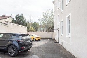 Ein Parkplatz mit zwei Autos, einem schwarzen SUV und einem gelben Sportwagen, vor einem Gebäude mit weißen Wänden und einem Ziegeldach.