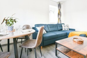 Ett vardagsrum med en blå soffa, ett matbord med stolar och ett soffbord.
