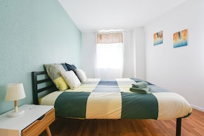 Ein Schlafzimmer mit einem Bett, einem Nachttisch, einer Lampe und einem Fenster mit Vorhängen.