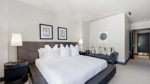 Ein modernes Hotelzimmer mit einem großen Bett, einer Couch, zwei gerahmten Kunstwerken und einer Tür.