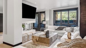 Ein modernes Wohnzimmer mit großem Fenster, einem an der Wand befestigten Flachbildfernseher, einem weißen Sofa und einem Couchtisch.