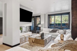 A modern living room with a large window, a flat-screen TV mounted on the wall, a white sofa, and a coffee table. - Solaris 4A East - 4 Bedroom + Den (Vail)