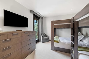 A modern bedroom with a flat-screen TV, a wooden dresser, a bunk bed, and a window with curtains. - Solaris 4A East - 4 Bedroom + Den (Vail)