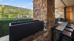 Ein Balkon mit Steinmauer, einem schwarzen Pflanztopf und einem Holztisch mit Stühlen.