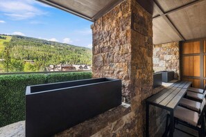 A balcony with a stone wall, a black planter, and a wooden table with chairs. - Solaris 4A East - 4 Bedroom + Den (Vail)