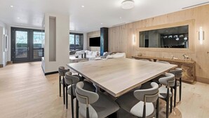 Ein geräumiger Essbereich mit einem großen Holztisch und modernen Stühlen, eine Küche mit einem großen Fenster sowie ein Wohnbereich mit einer Couch und einem Fernseher.