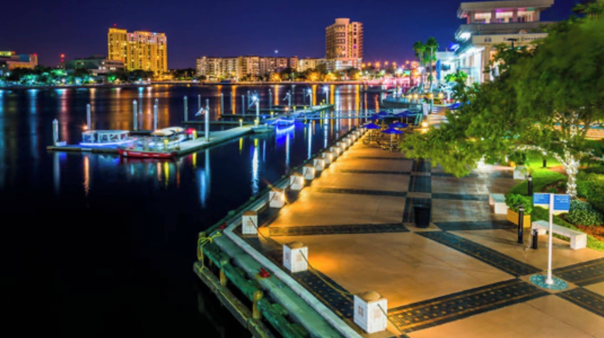 Un paseo marítimo con muelle, reflejos en el agua y edificios al fondo.