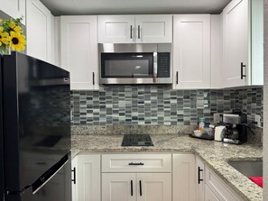 A kitchen with white cabinets, a stainless steel microwave, a black refrigerator, a granite countertop, and a coffee maker. - My Lily Apartment 8 Min Stadium 10 Airport 12 Zoo (Tampa)