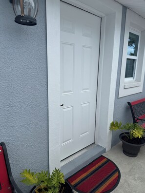 A white door with a textured gray wall, a red bench, and two potted plants. - My Lily Apartment 8 Min Stadium 10 Airport 12 Zoo (Tampa)
