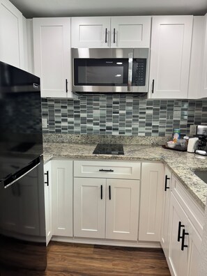 A kitchen with white cabinets, a stainless steel microwave, a black refrigerator, and a tiled backsplash. - My Lily Apartment 8 Min Stadium 10 Airport 12 Zoo (Tampa)