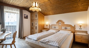 Ein Schlafzimmer mit zwei Betten, Holz-Kopfteilen, einer Holzbalkendecke, einem Fenster mit Vorhängen und einem kleinen Tisch mit einem Stuhl.