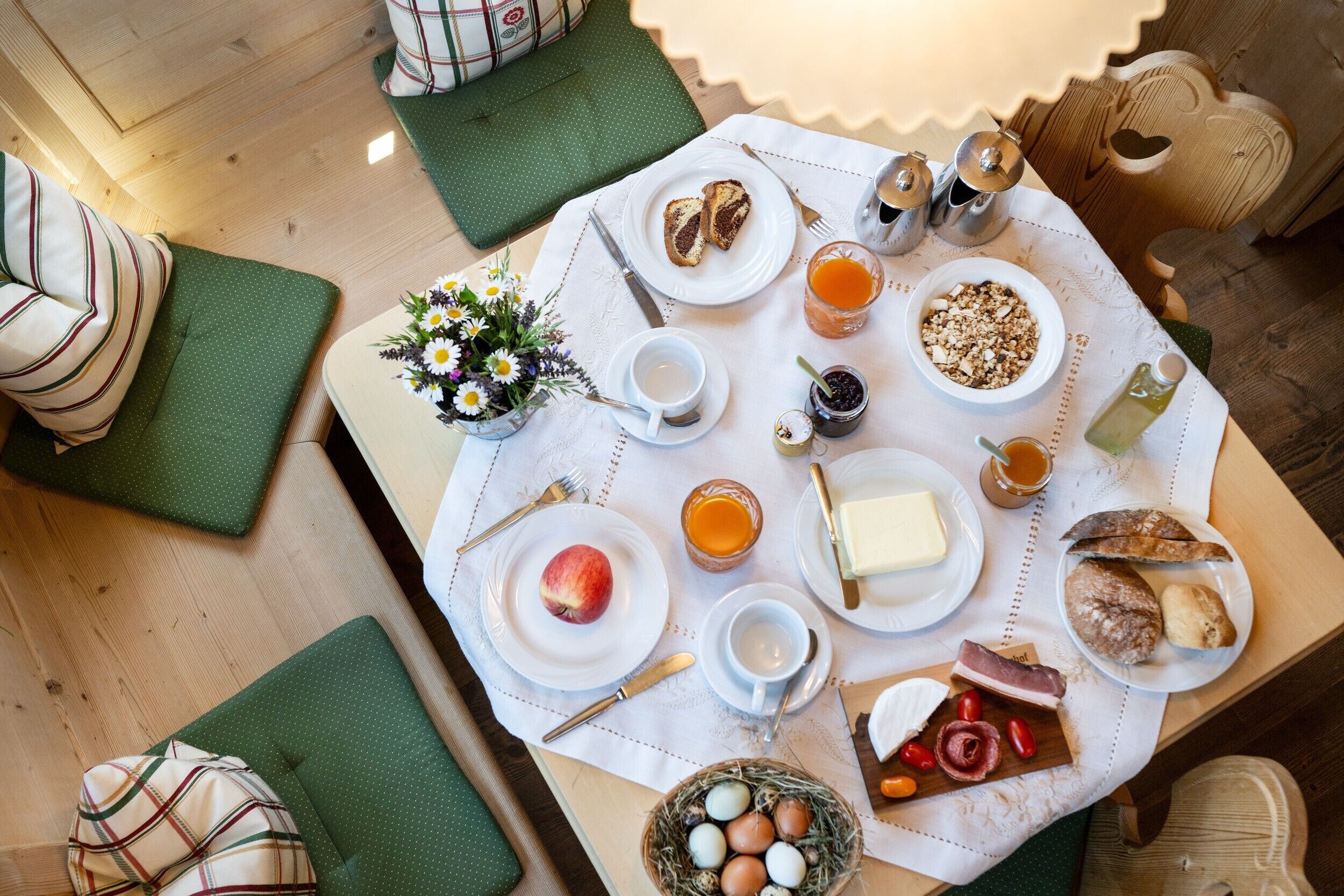 A breakfast setting with a variety of food items and drinks on a table, including bread, eggs, and a fruit.