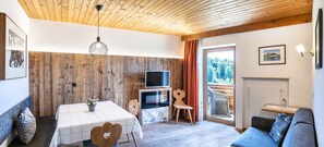 Ein gemütliches Zimmer mit Holzbalkendecke, Kamin, Fernseher und einer Couch.