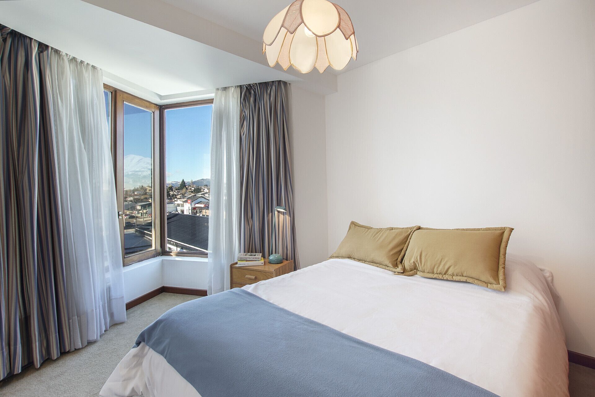 Een hotelkamer met een groot bed, een nachtkastje, een lamp en uitzicht op een stad door een raam.