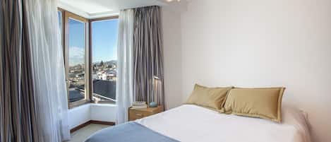 Habitació d'hotel amb un llit gran, una tauleta de nit, una làmpada i vista a una vila per la finestra.
