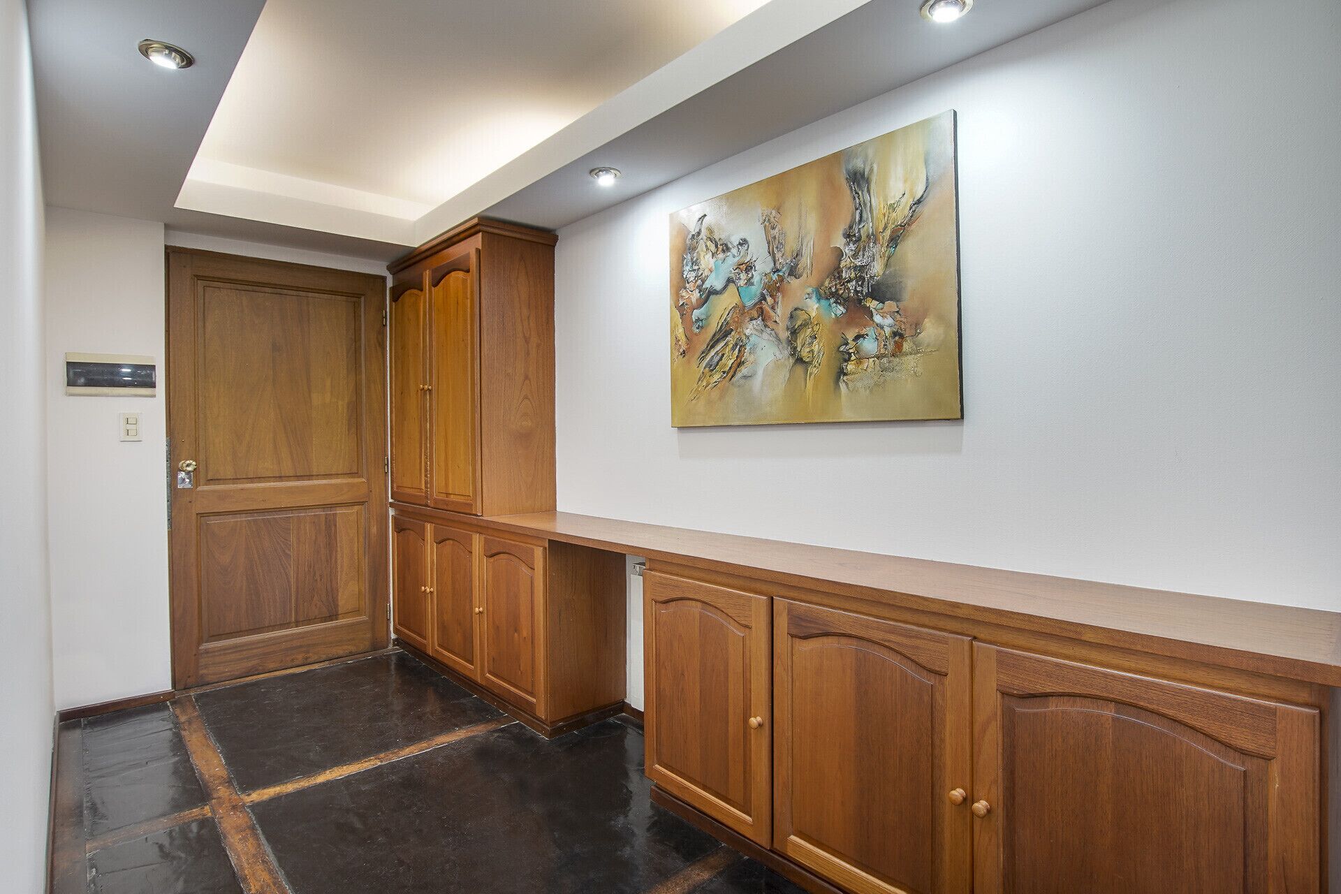 Un couloir avec des armoires en bois et un grand tableau abstrait accroché au mur.