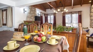 Un comedor con pared de piedra, sillas de madera, una mesa dispuesta con platos, vasos y frutas.