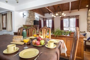A dining area with a stone wall, wooden chairs, a table set with plates, glasses, and fruits.