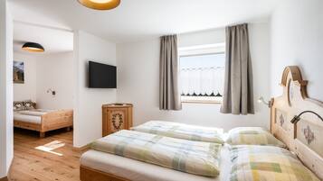 A bedroom with a wooden bed, a bedside table, a TV mounted on the wall, and a window with curtains.