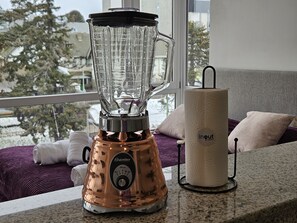 A kitchen with a blender on the counter, a roll of paper towels, and a window with a view of trees and buildings. - Canto de Aguila Bariloche (San Carlos de Bariloche)