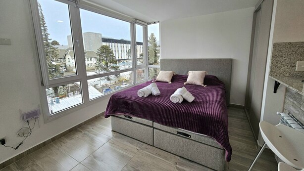 A bedroom with a large window, a bed with a headboard, and a built-in bench. - Canto de Aguila Bariloche (San Carlos de Bariloche)