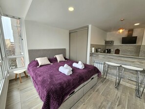 Ein modernes Hotelzimmer mit einem großen Bett, einem Einbauschrank, einer Küchenzeile und Blick auf die Stadt.
