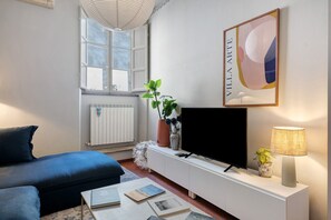 Uma sala de estar moderna com um sofá, uma televisão de tela plana, uma mesa de console branca e uma janela com vista.