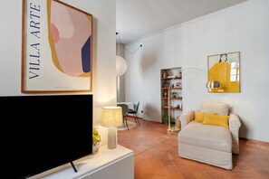 A living room with a flat-screen TV, a sofa with yellow cushions, a lamp, and a bookshelf. - 'Classy City-center Oasis' Apartment with Wi-Fi and Air Conditioning (Lucca)