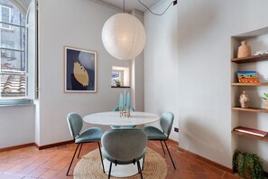 Uma sala de jantar com uma mesa redonda, cadeiras, um lustre e uma prateleira na parede com objetos decorativos.